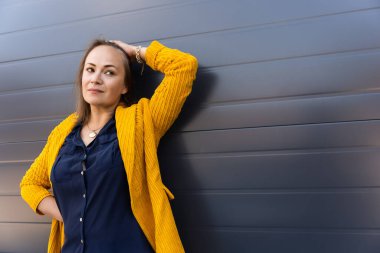 Gri arka plana yaslanmış 40 yaşında rahat bir kadın..