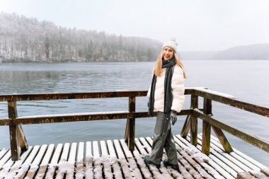 Gülümseyen kadın, karlı kış manzarasında tahta bir iskelede duruyor..