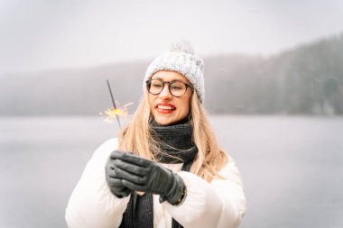 Karlı bir günde elinde bir maytap tutarken gülümseyen bir kadın..