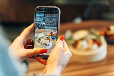 Modern bir restoranda Asya sokak yemeklerinin akıllı telefonuyla fotoğrafını çeken bir kadın..