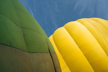 Açık mavi gökyüzüne karşı sarı ve yeşil sıcak hava balonları, kısmi manzara.