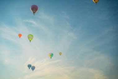 Açık mavi gökyüzünde yükselen renkli sıcak hava balonları.