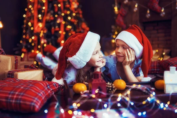 Dzieci Piżamach Czapkach Mikołajów Leżące Podłodze Patrząc Siebie Pobliżu Choinki — Zdjęcie stockowe