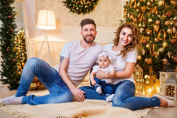 stock image Happy family of mother, father and little baby girl sitting near Christmas tree on the floor in decorated interior. Celebrating Christmas. 