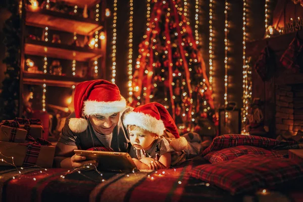 Vader Met Zoontje Pyjama Santas Hoedjes Thuis Bed Gebruikt Digitale — Stockfoto