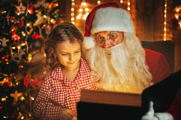 Święty Mikołaj Czyta Bajki Bożonarodzeniowe Dziewczynce Piżamie Siedząc Przy Kominku — Zdjęcie stockowe