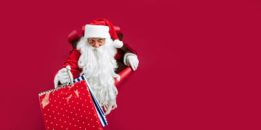 Noel Baba elinde alışveriş poşetleri tutarken kırmızı kağıttaki delikten geçmeyi bekliyor. Noel satışları. Yeni yıl alışverişi. Kara Cuma 