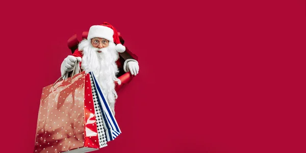 Święty Mikołaj Patrząc Przodu Przez Dziurę Czerwonym Papierze Trzymając Torby — Zdjęcie stockowe