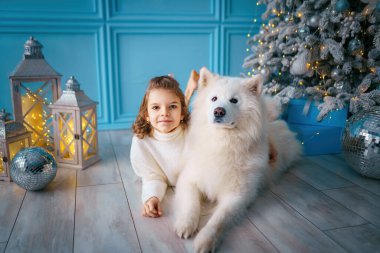 Mutlu küçük kız, salonda noel ağacının yanında hastalıklı köpekle birlikte yatıyor. Yeni yıl konsepti. Noel süslemeleri 