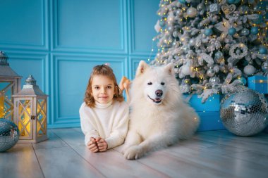  Küçük kız salonda noel ağacının yanında hasta köpekle birlikte yatıyor. Yeni yıl konsepti. Noel süslemeleri 