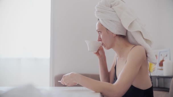 頭の上にタオルでシャワー後の美しい若い女性は キッチンで自宅でコーヒーや紅茶を飲みます — ストック動画
