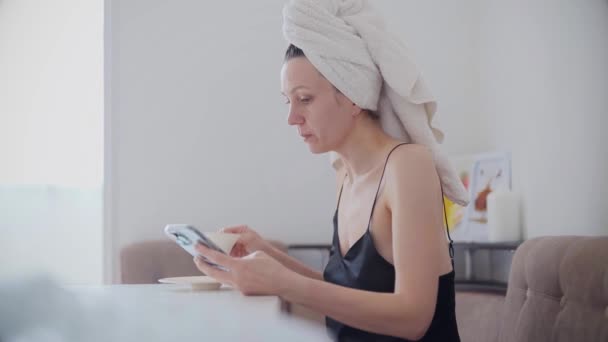 漂亮的年轻女子在厨房洗澡后喝着早上的咖啡 在智能手机上冲浪 — 图库视频影像