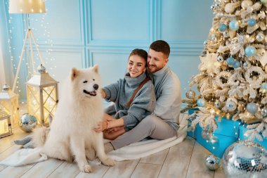 Mutlu çift evde oturup Noel ağacının yanında sarılıyor. Ocak, ev kıyafetleri ve kazaklar. konfor ve kalplerin sıcaklığı