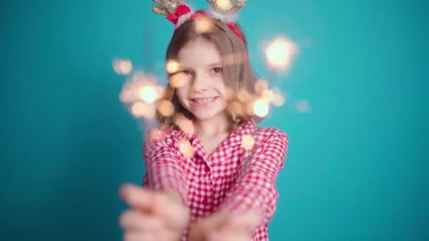 穿着睡衣的小女孩笑得很可爱 她在镜头前拿着闪闪发光的东西 背景是彩色的 圣诞节的概念 — 图库视频影像