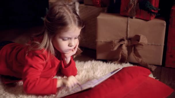 クリスマスプレゼントの近くのカーペットの上に横になり タブレットを使用している少女 カメラの動き — ストック動画