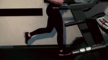 Spor salonunda koşu bandında koşan fitness kızı, spor kulübünde kardiyo eğitimi alan. Ağır çekim. Kamera hareket ediyor 