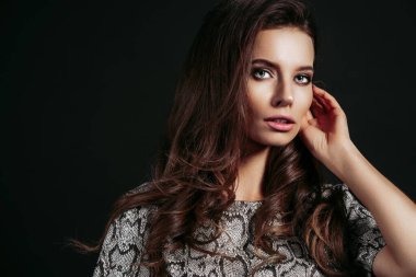 Siyah arka planda izole edilmiş yılan desenli elbise giymiş güzel uzun saçlı esmer genç kadın kameraya bakıyor. Güzel saç stili portresi.. 