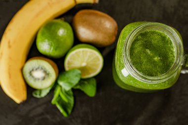 Cam kavanozdaki yeşil smoothie ve malzemelerin yukarıdan görünüşü: baban, kivi, limon, ahşap arka planda yeşillik. İyi yemek konsepti. Seçici Odaklanma 