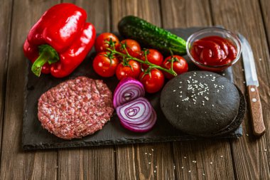 Bıçaklı, çiğ et köfteli, soğanlı, domatesli, ketçaplı, dolma biberli, salatalıklı siyah burger için taze malzemeler. Lezzetli yemek. Ev yapımı yemek. 