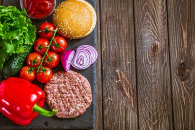 Siyah taş tahtada sığır burger, çiğ et köftesi, soğan, marul, domates, ketçap, dolma biber. Tahta masa. Lezzetli yemek konsepti. Metin için boşluk 