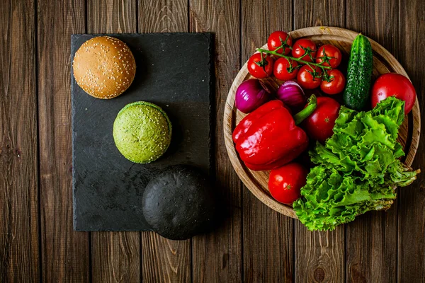 Top down view of ingredients for three vegetarian hamburgers on the wooden table. Black, green, yellow buns. Delicious food. Vegetarian food