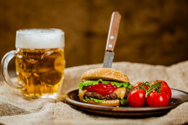 Köy ahşap servis masasında bıçaklı taze ev yapımı sığır burger ve bir bardak bira. Seçici odak. 