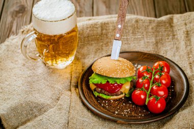 Ev yapımı taze sığır etli burgerin üst görüntüsü. Kırsal ahşap servis masasında bıçak ve bir bardak birayla. Seçici odak. 