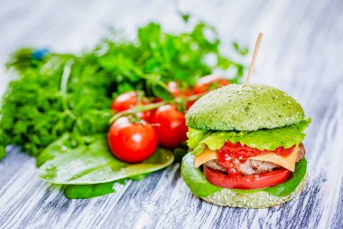 Yeşil ekmekli hamburger, yapay et ve beyaz ahşap arka planda taze sebzeler. Vejetaryen yemeği. 