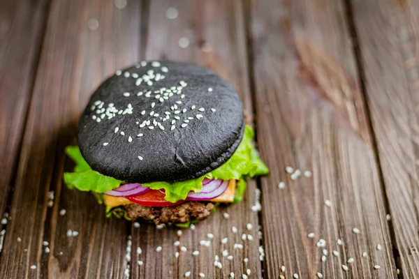 From above view of burger with black bun with artificial meat and fresh greenery and veggies on wooden table. Vegetarian food. Selective focus .