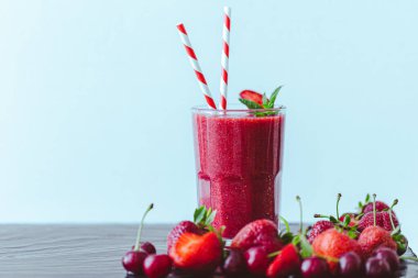 Taze çilek suyu ya da bardakta saman ve mavi arka planda taze çilek ve kirazlı smoothie. Seçici odaklanma. Vejetaryen yemeği. Sağlıklı yiyecekler. Vitamin yiyeceği. 