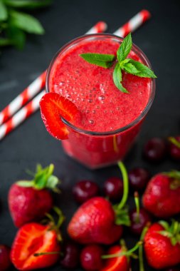 Üst görüntüde taze çilek suyu ya da bardakta taze çilek ve kirazlı buzlu smoothie var. Seçici odaklanma. Vejetaryen yemeği. Sağlıklı yiyecekler. Vitamin yiyeceği. 
