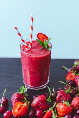 Taze çilek suyu ya da bardakta saman ve mavi arka planda taze çilek ve kirazlı smoothie. Seçici odaklanma. Vejetaryen yemeği. Sağlıklı yiyecekler. Vitamin yiyeceği. 
