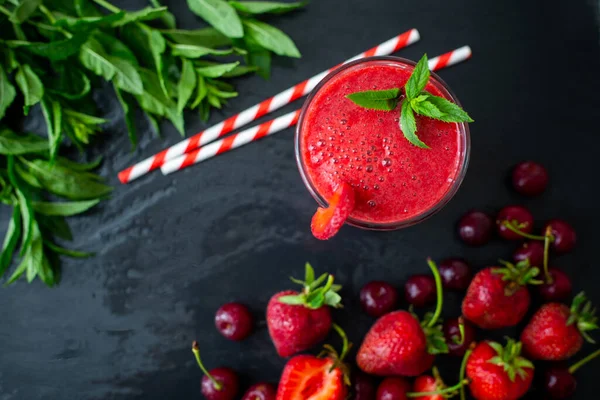 Top down view of fresh berry juice or smoothie with straw in glass with fresh strawberries and cherries on dark background. Vegetarian food. Healthy food. Vitamin food. Selective focus