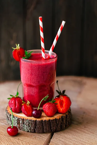 Fresh tasty berry juice or smoothie with straw in glass with fresh strawberries and cherries on wooden background. Selective focus. Vegetarian food. Healthy food. Vitamin food