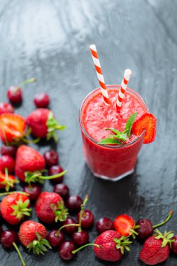 Yukarıdan bakıldığında taze çilek suyu ya da bardakta saman ve koyu arkaplanda taze çilek ve kirazlı smoothie görülebilir. Seçici odaklanma. Vejetaryen yemeği. Sağlıklı yiyecekler. Vitamin yiyeceği. 