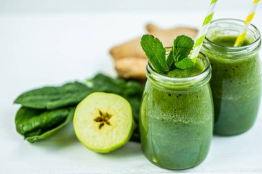 Yeşil ıspanak, meyve suyu ve ahşap kırsal masada bulunan malzemelerle dolu pipetli kavanozlar. Yeşil sağlıklı yiyecek, vejetaryen, temiz yeme konsepti. 