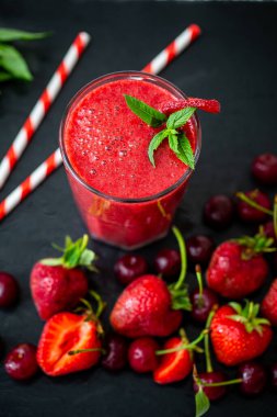 Yukarıdan bakıldığında, taze nane, çilek ve kirazlı bardakta saman bulunan taze meyve suyu veya smoothie. Seçici odaklanma. Vejetaryen yemeği. Sağlıklı yiyecekler. Vitamin yiyeceği. 