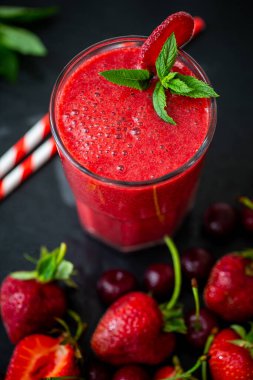 Taze çilek suyu ya da bardakta taze çilek ve siyah arka planda kirazlı buzlu smoothie yakından görülüyor. Seçici odaklanma. Vejetaryen yemeği. Sağlıklı yiyecekler. Vitamin yiyeceği. 