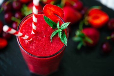 Taze çilek suyu ya da bardakta taze çilek ve siyah arka planda kirazlı buzlu smoothie yakından görülüyor. Seçici odaklanma. Vejetaryen yemeği. Sağlıklı yiyecekler. Vitamin yiyeceği. 
