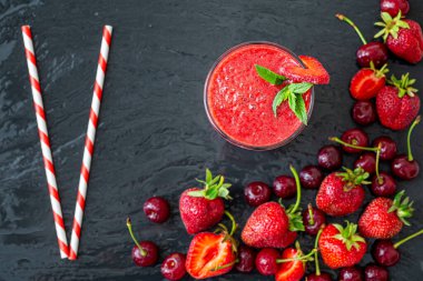 Yukardan taze çilek suyu ya da bardakta saman ve koyu arkaplanda taze çilek ve kirazlı smoothie. Vejetaryen yemeği. Sağlıklı yiyecekler. Vitamin yiyeceği. 