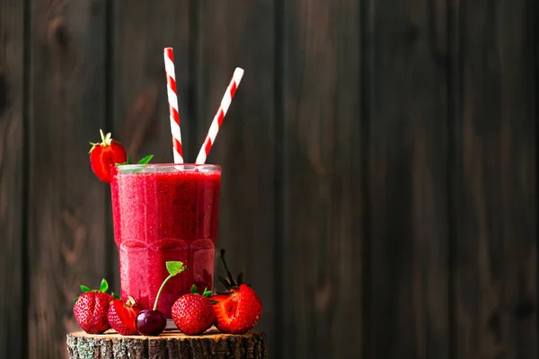 Fresh berry juice or smoothie with straw in glass with fresh strawberries and cherries on wooden background. Selective focus. Vegetarian food. Healthy food. Vitamin food