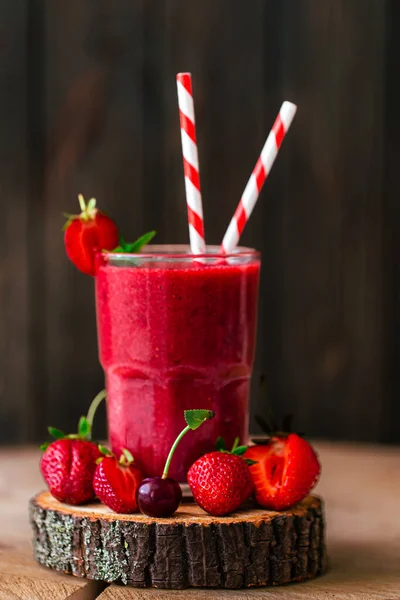 Side view of fresh berry juice or smoothie with straw in glass with fresh strawberries and cherries on wooden background. Selective focus. Vegetarian food. Healthy food. Vitamin food