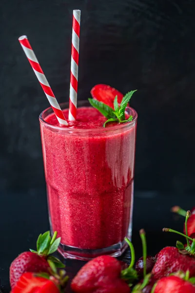 Side view of fresh berry juice or smoothie with straw in glass with fresh strawberries and cherries on dark background. Selective focus. Vegetarian food. Healthy food. Vitamin food