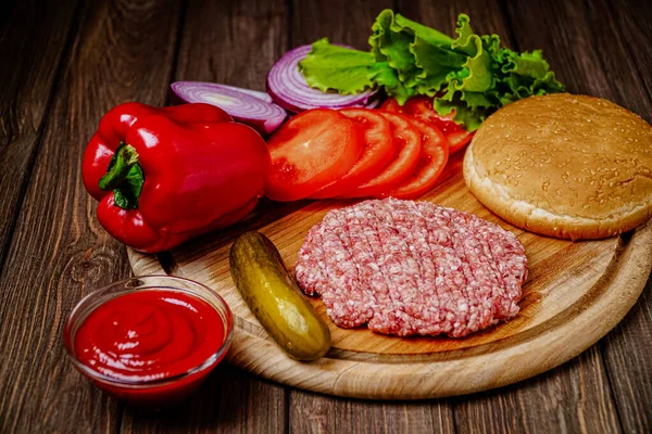 From above view of process of making hamburger with vegetables, bun and artificial meat on wooden board. Vegetarian food .