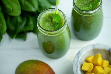 Mangolu yeşil smoothie, ahşap beyaz masada ıspanak. Sağlıklı yiyecekler. Vejetaryen diyeti. Seçici odak 
