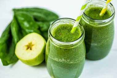 Yukarıdan bakıldığında yeşil ıspanak, meyve suyu ve ahşap beyaz masada bulunan malzemelerle dolu pipetli kavanozlar. Yeşil sağlıklı yiyecek, vejetaryen, temiz yeme konsepti. 