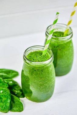 Yeşil smoothie ve ıspanak ahşap beyaz masa ile doldurulmuş pipetli gözlük kavanozları. Yeşil sağlıklı yemek, vejetaryen, temiz yeme konsepti. Boşluğu kopyala 