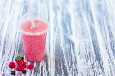 Kapalı fincanda böğürtlenli, böğürtlenli, ahudutlenli ve ahşap zemin üzümlü plastik bardakta meyveli milkshake. Seçici odaklanma. Sağlıklı beslenme. Vejetaryen diyeti. Boşluğu Kopyala 