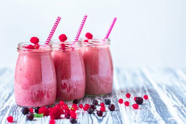 Kadeh kavanozunda üç meyveli milkshake, içinde pipetle yaban mersini, ahududu, ahşap zemin üzümü. Seçici odaklanma. Sağlıklı beslenme. Vejetaryen diyeti. Boşluğu Kopyala 