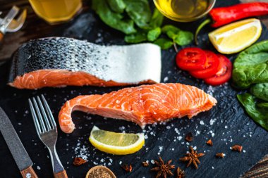 Limon, ıspanak, baharat, zeytinyağı ve levhada pişirmeye hazır kırmızı biberli çiğ somon balığı filetosu. Ev yapımı yemek. Seçici odak 